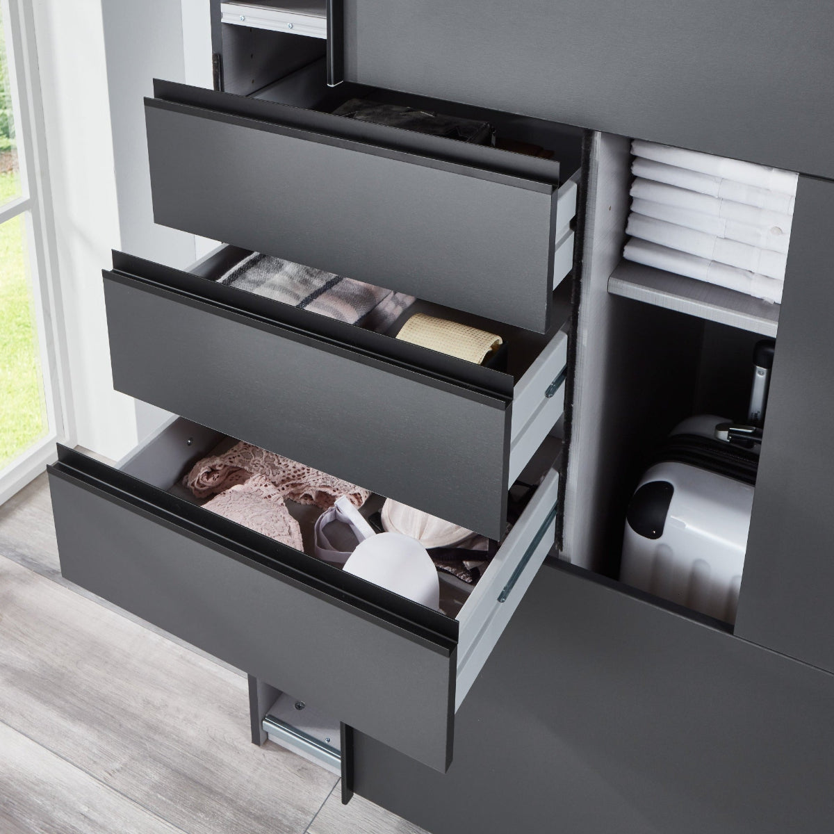 Gray dresser with open drawers in a room with a window showing greenery